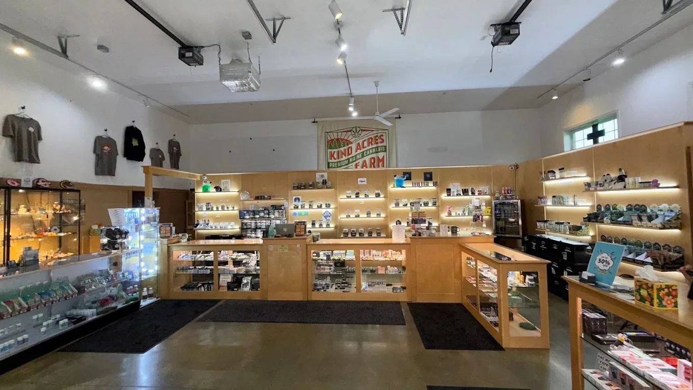 Inside Kind Acres Farm — warm-lit blond-wood shelves stocked with Maine cannabis under the KIND ACRES FARM · Premium Maine Cannabis banner