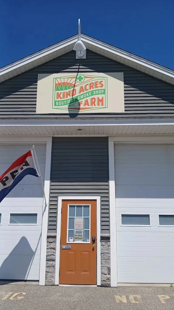 Kind Acres Farm storefront on a clear blue-sky day — sign in the gable, orange door, OPEN flag flying